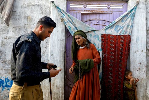 Edema Bibi, 66, an Afghan citizen, stands at the entrance of her house as a police officer checks her registration card, during a door-to-door search and verification drive for undocumented Afghan nationals, in an Afghan Camp on the outskirts of Karachi, Pakistan, November 21, 2023.