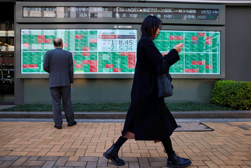 A woman walks past a man examining an electronic board showing Japan's Nikkei average and stock quotations outside a brokerage, in Tokyo, Japan, March 20, 2023.