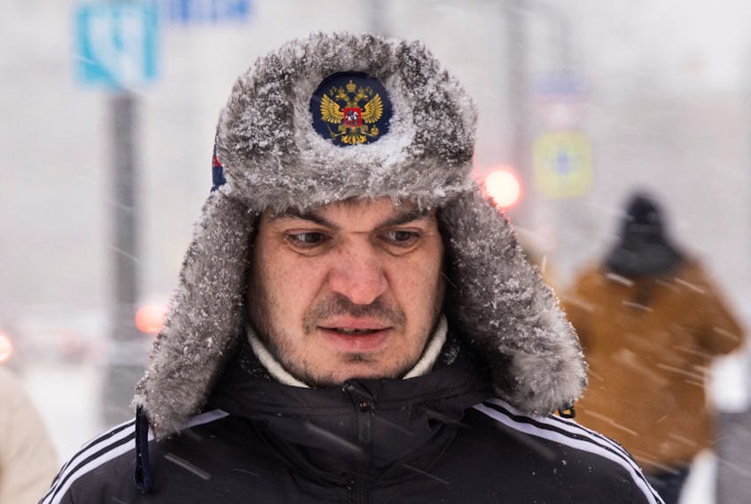 A man wearing a hat with Russian national coat of arms walks in the street during a heavy snowfall in Moscow, Russia December 3, 2023.