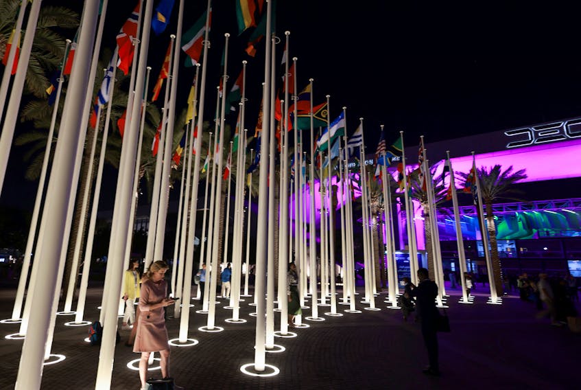 People stand near the flags at Dubai's Expo City during the United Nations Climate Change Conference (COP28) in Dubai, United Arab Emirates, December 4, 2023.