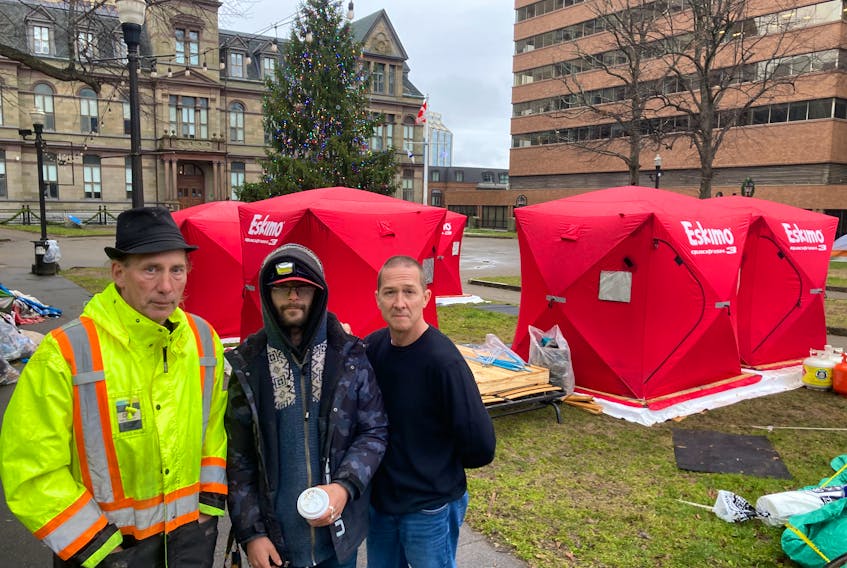 For the past two weeks Steve Wilsack, left, and Matt Grant, right, have been replacing tents with new heavy-duty shelters at the homeless camp site at Grand Parade in Halifax. They're shown with Michael Baker, who's living in one of the shelters. - Contributed
