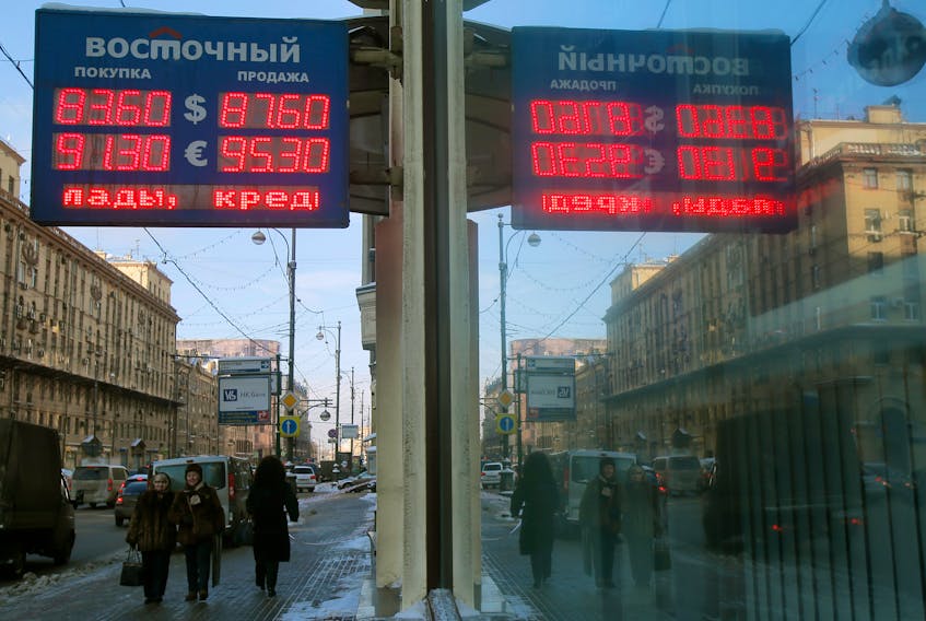 People walk near a board showing currency exchange rates of the U.S. dollar and euro against the rouble in Moscow, Russia, January 21, 2016.