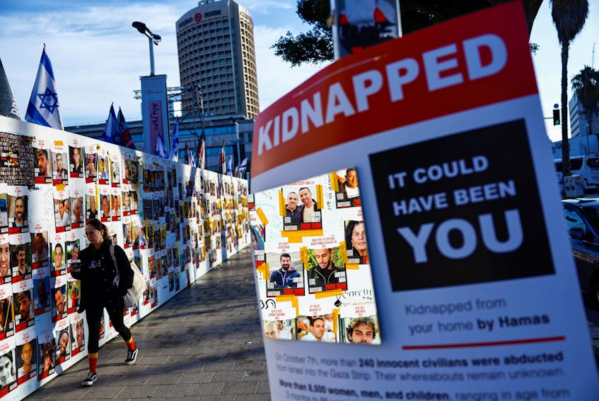 A woman walks past posters on a message board with pictures of hostages, who are being held in the Gaza Strip after they were seized by Hamas gunmen on October 7, as the country observes the Jewish festival Hanukkah amid the ongoing conflict between Israel and the Palestinian Islamist group Hamas, in Tel Aviv, Israel December 7, 2023.