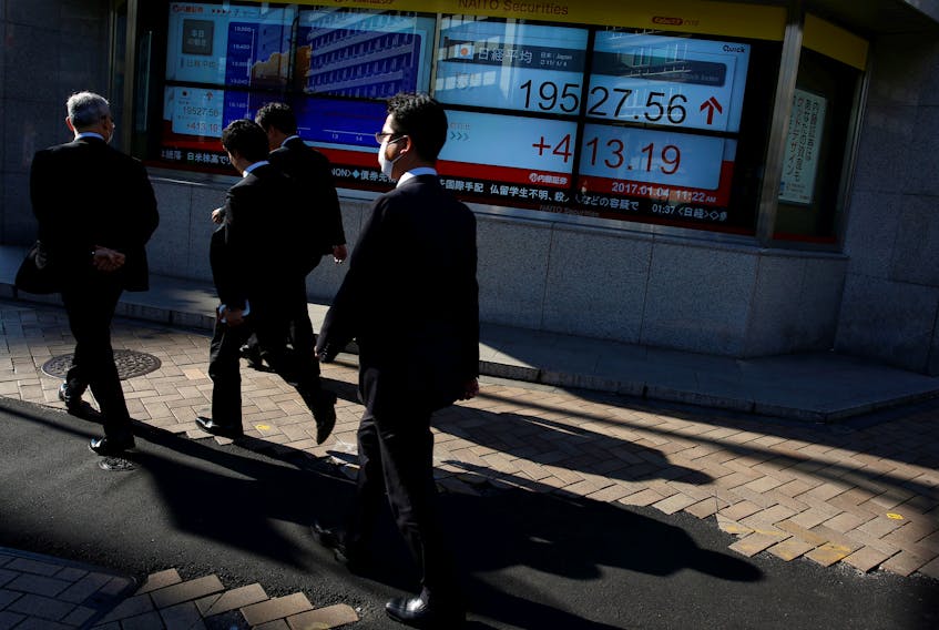 File photo: People walk past an electronic board showing stock prices outside a brokerage at a business district in Tokyo, Japan, January 4, 2017.