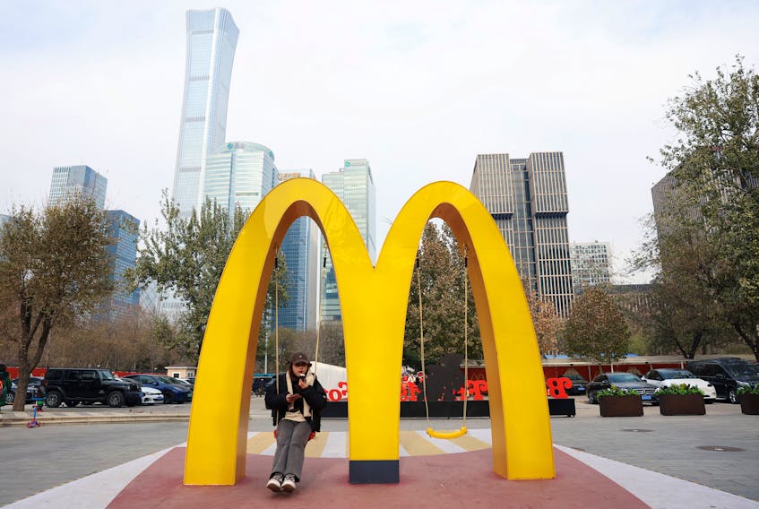 A woman sits on a swing attached to a giant sign of McDonald's, outside its themed exhibition in Beijing, China December 4, 2023.