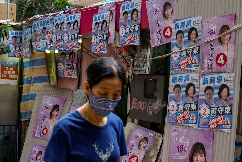 A woman walks past a vendor stall posted with campaign posters of district council election candidates in Hong Kong, China December 9, 2023.