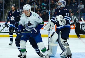 Vancouver Canucks forward Curtis Lazar, left, and Winnipeg Jets goalie Connor Hellebuyck look for the puck at the Canada Life Centre on Dec 29, 2022, in Winnipeg.