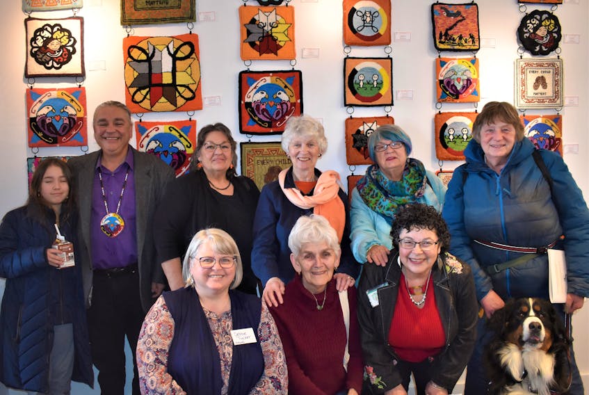 Coming together during a grand opening event earlier this month were participating Mi’kmaw artists and Rug Hooking Guild of Nova Scotia (RHGNS) members who participated in the Finding a Way Forward project. Pictured, with some of the artwork as a backdrop, are artist Lorne Julien and his granddaughter Grace (back, left), artist Noella Moore, RHGNS project organizer Ann Marie Harley, rug hooker Tanya McNutt, rug hooker Karen Stratton with her dog Bailey, RHGNS project organizer Debbie Tucker (front, left), and rug hookers Marilyn Rector and Ursula Gulliver. Richard MacKenzie