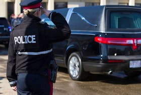 An Edmonton Police Service officer salutes as a procession arrives with the bodies of Const. Travis Jordan and Const. Brett Ryan at the Serenity Funeral Home in Edmonton on Tuesday. - David Bloom/Postmedia