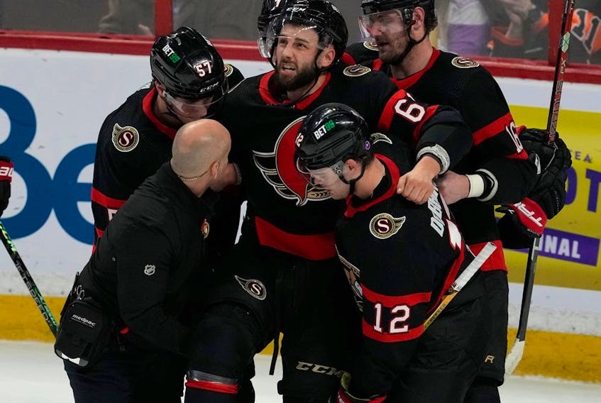 Senators teammates Shane Pinto, Alex DeBrincat and Austin Watson help Derick Brassard off the ice after he was injured during the second period of Thursday's home game against the Flyers.