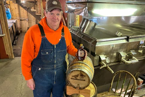 Steven Thompson of the Bouchard-Thompson maple camp in Fenwick, near Amherst, with a bottle of his syrup on a Raging Crow barrel. Darrell Cole
