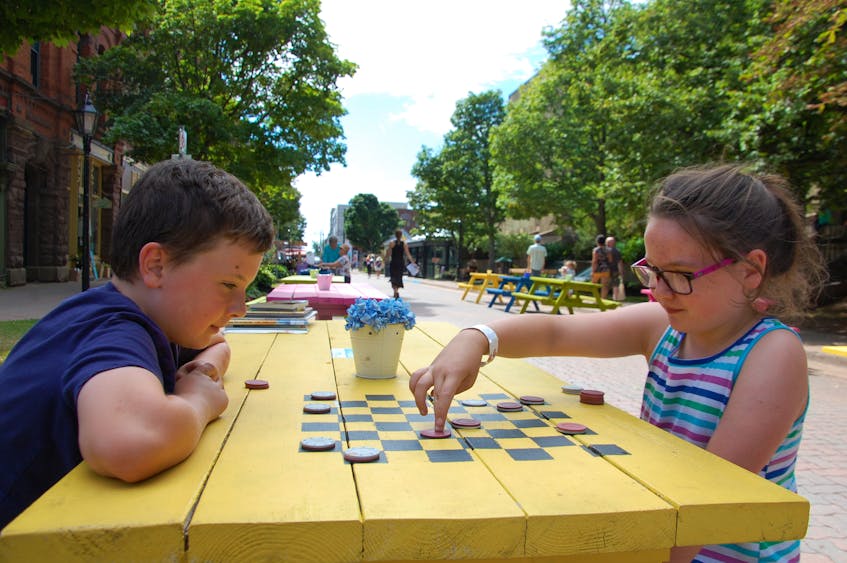 Children play a game of checkers in August 2019 on one of the picnic table boards set up along Victoria Row in Charlottetown. This is a local example of a pedestrian zone that could be replicated elsewhere in the city. 