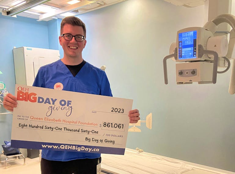 Queen Elizabeth Hospital medical radiation technologist Nicholas Lynch holds the QEH Big Day of Giving grand fundraising total of $861,061. The x-ray machine is among the equipment pieces that will be replaced with the donations. Contributed