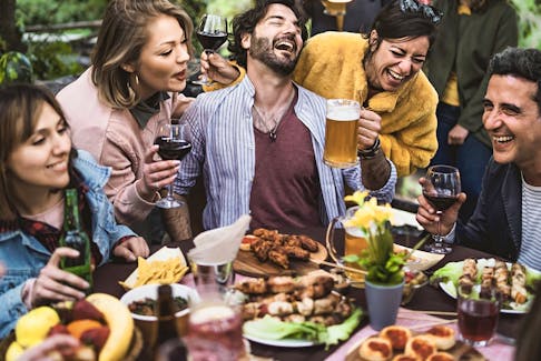Group of friends laughing, drinking beer and wine and eating together.
