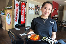 Mary Grace Gomez, co-owner of Omma's Korean Bar BQ and Grill in Sydney, stands in the dining room on Wednesday with two authentic dishes — kimbap in her right hand and tteokbokki, a vegetarian spicy rice cake meal. NICOLE SULLIVAN/CAPE BRETON POST