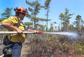 Department of Natural Resources and Renewables firefighter Walter Scott of Churchover, Shelburne County, sprays the ground while the water bomber flies by to dump a load of water on the fire. COMMUNICATIONS NOVA SCOTIA