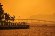  A person travels in a boat past people walking on the boardwalk as smoke from the McDougall Creek wildfire blankets the area on Okanagan Lake, in Kelowna, B.C., Friday, Aug. 18, 2023.