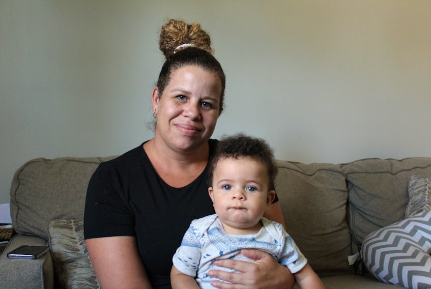 Destiny Beals sits on the couch in her living room, holding her 7-month-old son who desperately wants to escape her grasp.
