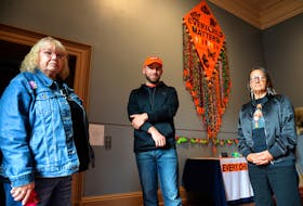Non-status Mi'lmaw elders Millie Renouf (left) and Sylvia Murphy stand with artist Justin Squires near an piece of art made up of coloured squares of felt that symbolize missing residential school victims.

Keith Gosse/The Telegram