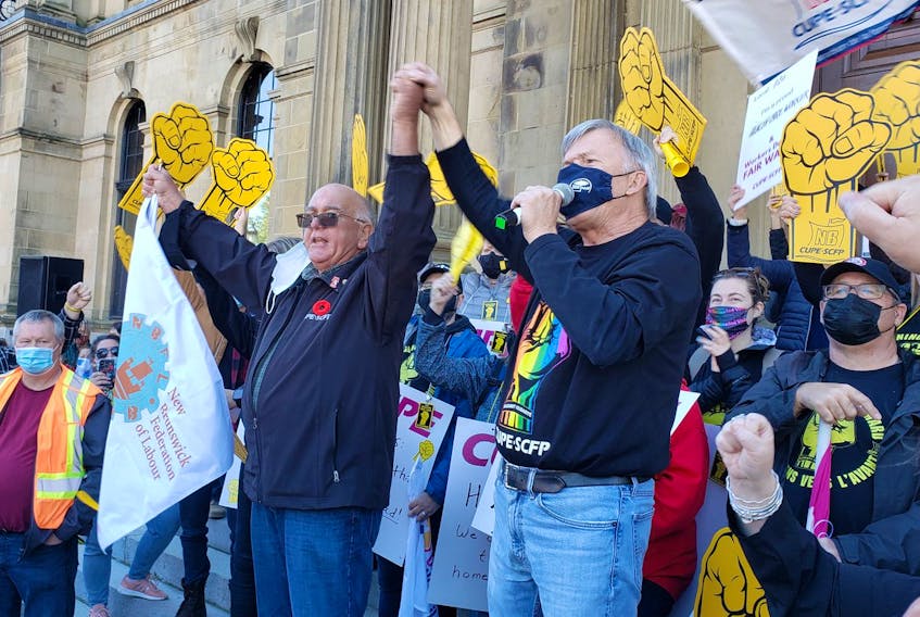 Danny Légère, left, who heads the New Brunswick Federation of Labour, holds hands with Stephen Drost, the local president of the Canadian Union of Public Employees, in front of the provincial legislature during a 2021 work stoppage. (The Daily Gleaner)