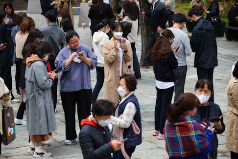 Office workers look at their mobile phones to check the local online banking app Toss as they gather at Seoul Museum of Art during a lunch break in Seoul, South Korea, April 13, 2023. 