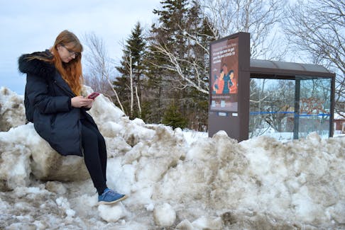 Emma Martens found a comfortable perch on top of a snowbank as she waited for the bus to pick her up on Alexandra Street in Sydney on Tuesday. Transit Cape Breton resumed all routes except for Route 15 following the record-breaking snowstorm. Due to ongoing winter conditions, people should expect delays. Chris Connors/Cape Breton Post