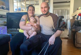Charisa Lykow, right, her husband Nathaniel and their daughter Aliza, sit in their Summerside living room. The couple had to rearrange their furniture to make the house accessible for Nathaniel, following an operation to amputate his right leg below the knee. – Kristin Gardiner/SaltWire