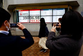 People using their smartphones take photos of electronic screens displaying Japan's Nikkei share average, which surged past an all-time record high scaled in December 1989, outside a brokerage in Tokyo, Japan February 22, 2024.