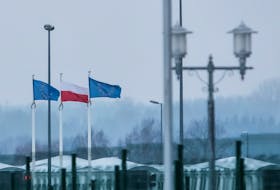 A view from the Belarusian side of the frontier shows Polish and EU flags behind a fence at Bruzgi-Kuznica checkpoint on the Belarusian-Polish border amid the migrant crisis in the Grodno region, Belarus, December 23, 2021.