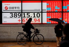 A cyclist and passersby pass in front of electronic screens displaying Japan's Nikkei share average outside a brokerage in Tokyo, Japan February 22, 2024.
