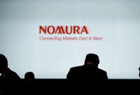 Investors stand in front of a screen showing the logo of Nomura Holdings in Tokyo, Japan, December 1, 2015. 