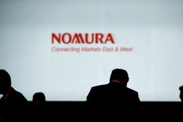 Investors stand in front of a screen showing the logo of Nomura Holdings in Tokyo, Japan, December 1, 2015. 