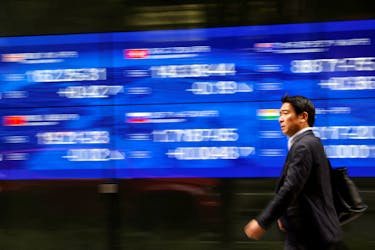 A passerby walks past an electric monitor displaying various countries' stock price index outside a bank in Tokyo, Japan, March 22, 2023.