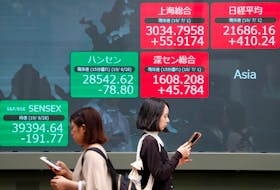 Passerbys walk past an electric screen showing Asian markets indices outside a brokerage in Tokyo, Japan, July 1, 2019. 