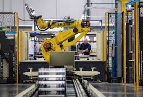 A factory worker works on an aircraft part, as the robot arm of an automated five-axis cell operates autonomously nearby, at Abipa Canada, in Boisbriand, Quebec, Canada May 10, 2023.