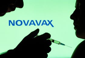People pose with syringe with needle in front of displayed Novavax logo in this illustration taken, December 11, 2021.