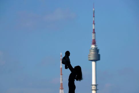 A woman holding up her baby is silhouetted against the backdrop of N Seoul Tower, commonly known as Namsan Tower, in Seoul, South Korea, October 2, 2018.  