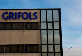 A plane flies behind an office and logistics building of Spanish pharmaceuticals company Grifols in Coslada, near Madrid, Spain, January 9, 2024.