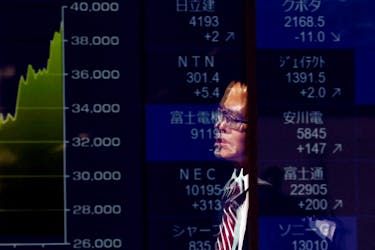 A passerby is reflected on an electronic screen displaying a graph showing recent Japan's Nikkei share average movements and stock prices as the share average hits a record high in Tokyo, Japan February 26, 2024. 