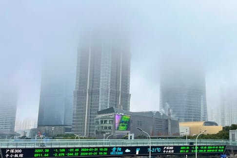 A display of stock information is seen in front of buildings in Lujiazui financial district that are shrouded in fog amid an orange alert for heavy fog in Shanghai, China January 31, 2024.