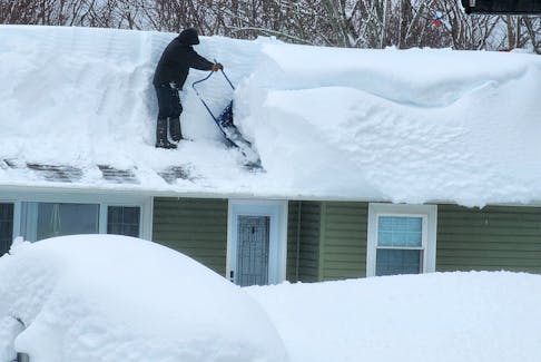 Todd Burke shovels snow off the roof of his home on Edgewood Drive in Sydney on Monday.  Mitchell Ferguson/Cape Breton Post