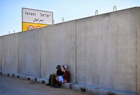 A woman holds a child as they sit by a wall, during a protest against the delivery of humanitarian aid to Gaza and demand the immediate release of hostages kidnapped on the deadly October 7 attack by Palestinian Islamist group Hamas, at the Kerem Shalom crossing, Israel, February 7, 2024.