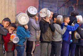 Palestinian children carry pots as they queue to receive food cooked by a charity kitchen, amid shortages in food supplies, as the conflict between Israel and Hamas continues, in Rafah in the southern Gaza Strip December 14, 2023.