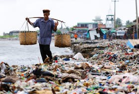 An elderly man carrying baskets walks through piles of trash, most of which is plastic and domestic waste, on a beach in Teluk fishing village, as high tides brought by erratic weather sweep trash to the shore in Pandeglang regency, Banten province, Indonesia, on March 15, 2024.