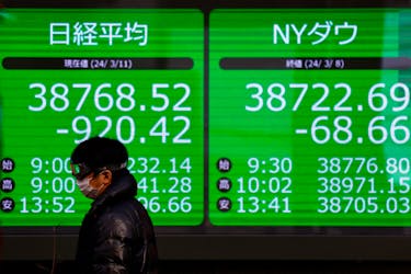 A passerby walks past an electric screen displaying Japan's Nikkei share average and the Dow Jones Industrial Average outside a brokerage in Tokyo, Japan March 11, 2024. 