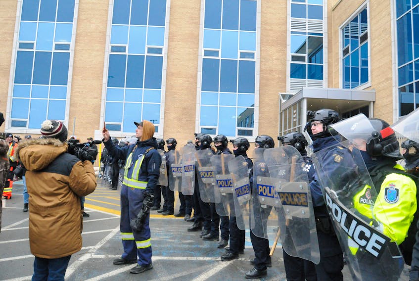 Despite a heavy police presence and hundreds of protesting fish harvesters for the second day in a row, employees were once again unable to enter the Confederation Building for work on Thursday, March 21, 2024. But the provincial Budget 2024 was read in the House of Assembly by finance minister Siobhan Coady on Thursday afternoon. RNC officers were joined with their comrades from the RCMP in preventing access to the employee and MHA entrance at the rear east entrance of the building. Above, fish harvester Jimmy Lee Ross of LaScie on the Baie Verte Peninsula, does a live hit as RNC and RCMP members dressed in protective gear, guard the doorway. All was quiet there as the protestors dispersed by mid-afternoon.
-Photo by Joe Gibbons/The Telegram