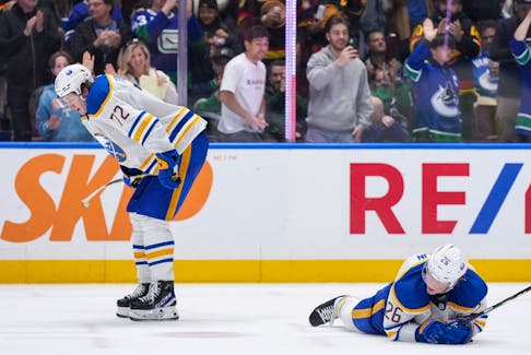 Buffalo Sabres' Rasmus Dahlin (26) lies on the ice as Tage Thompson (72) looks on while fans Vancouver Canucks celebrate.