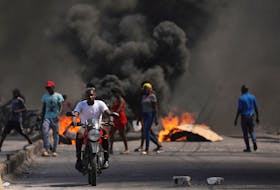 A man drives past a burning barricade during a protest against Prime Minister Ariel Henry's government and insecurity, in Port-au-Prince, Haiti March 1, 2024.