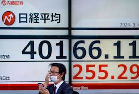 A man uses a smartphone in front of an electronic screen displaying Japan's Nikkei share average outside a brokerage in Tokyo, Japan March 4, 2024.