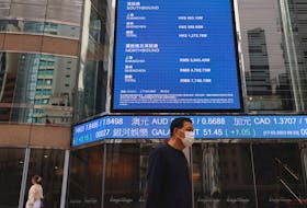 People walk past a screen displaying the Hang Seng Index at Central district, in Hong Kong, China March 17, 2023.